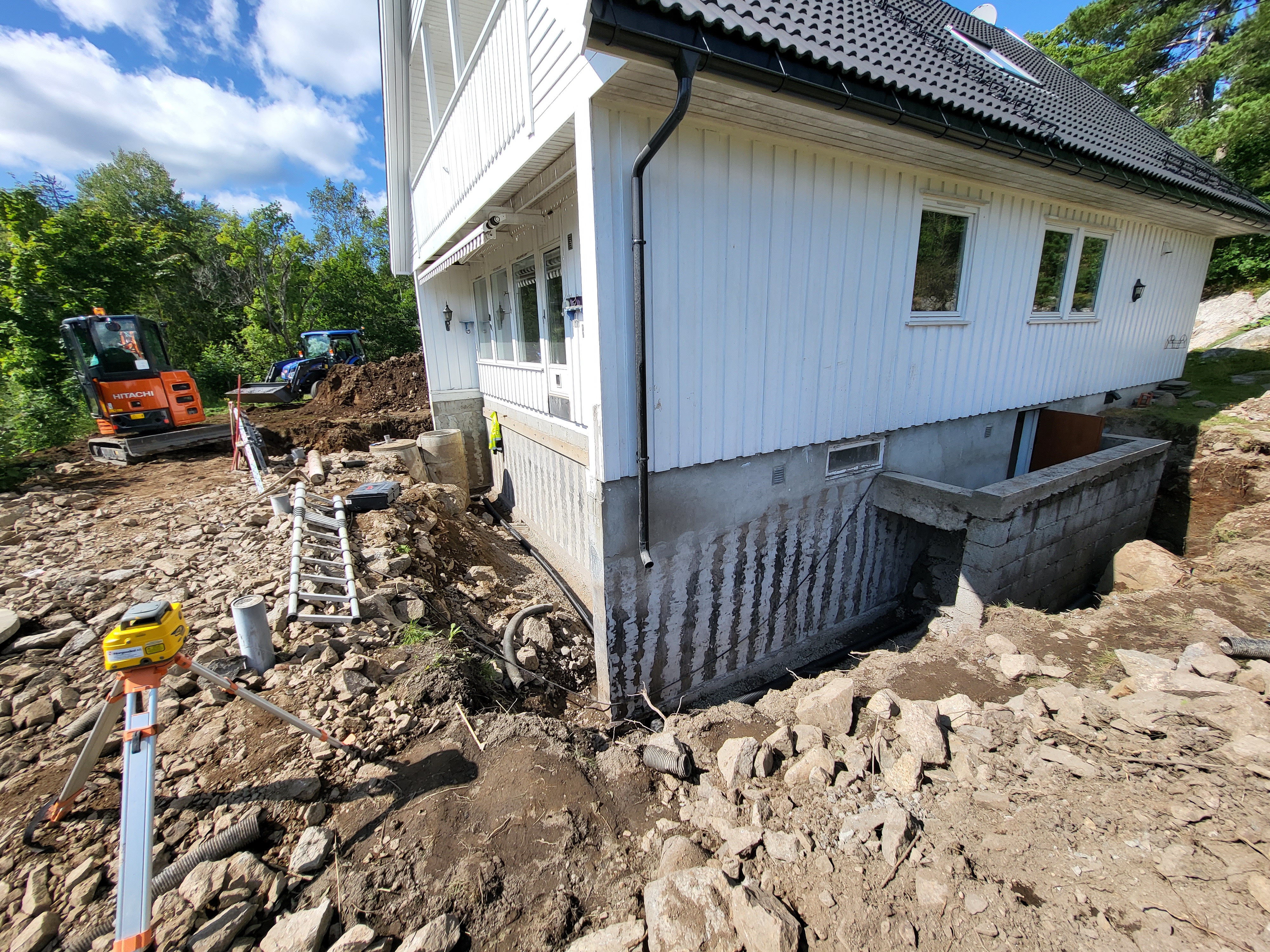 Gravemaskin i arbeid med drenering langs husvegg