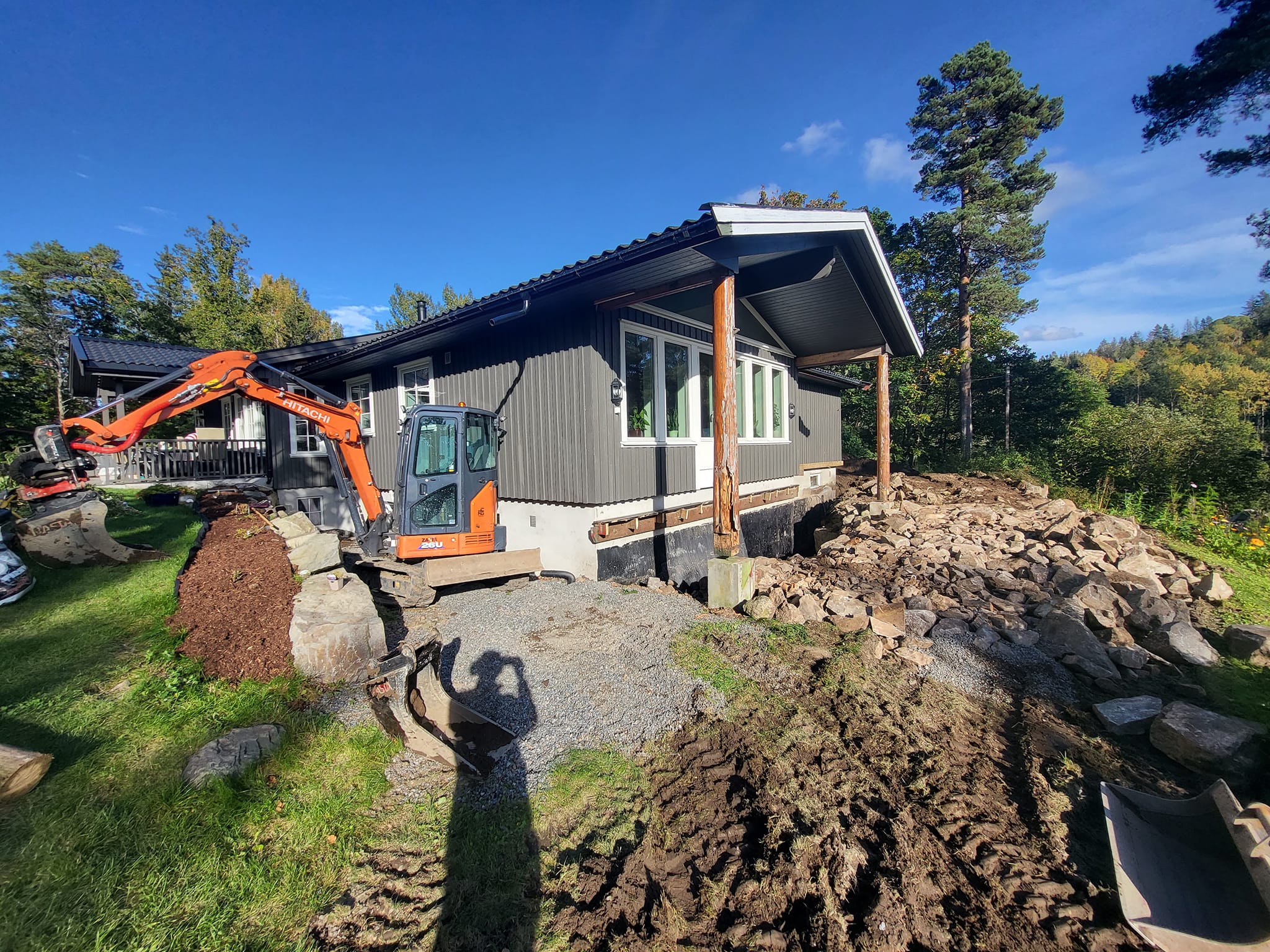 Gravemaskin jobber med drenering langs husvegg på enebolig